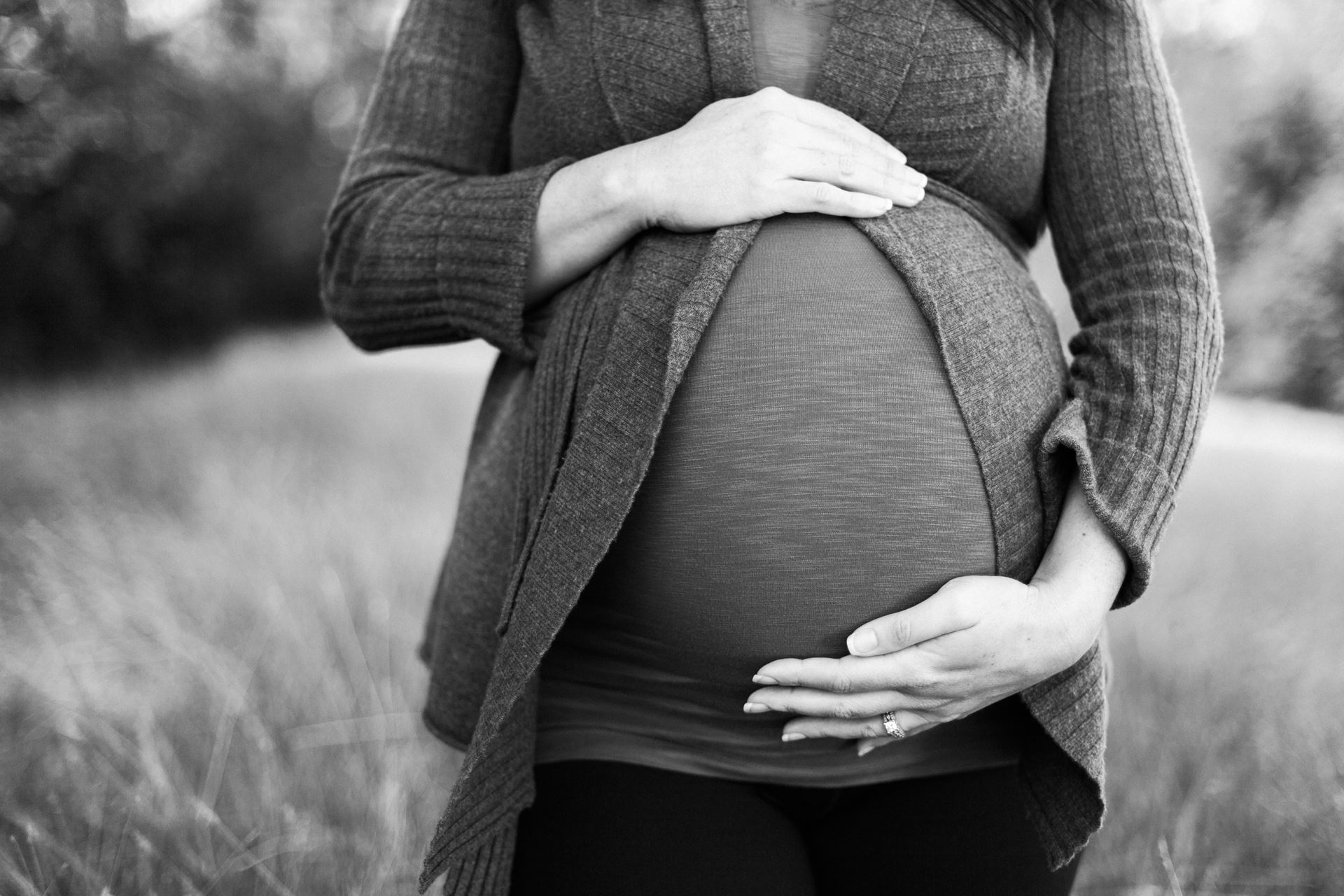 a grey scale image of pregnant person holding the top and bottom of her bump in a field